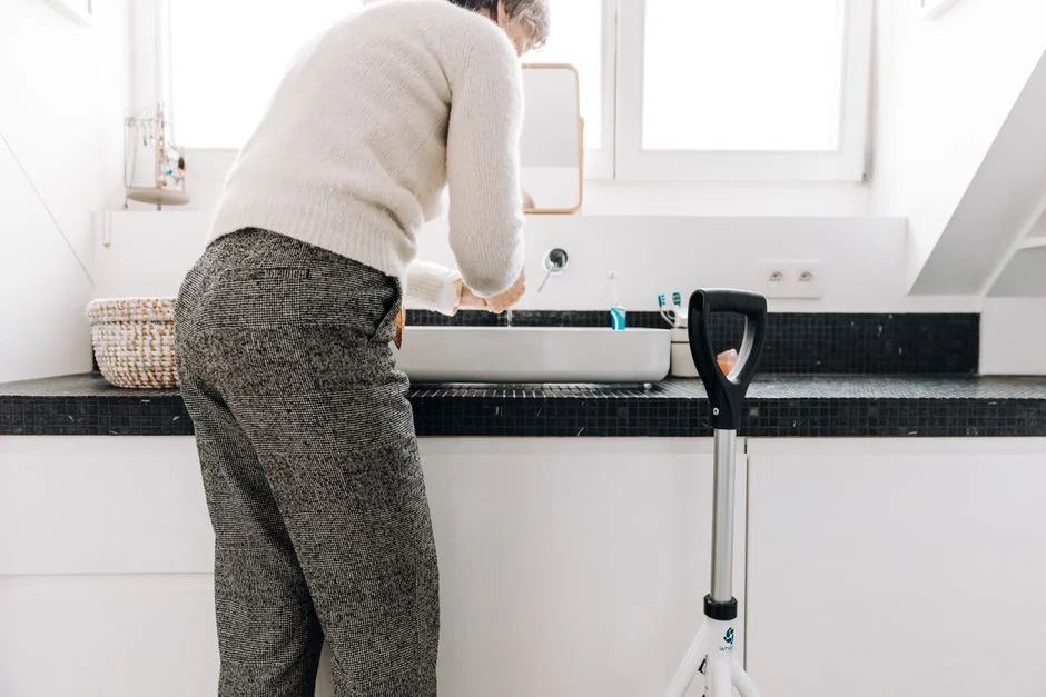 A woman cleaning the floor with a vacuum cleaner while a dog watches attentively. Indoor home setting.